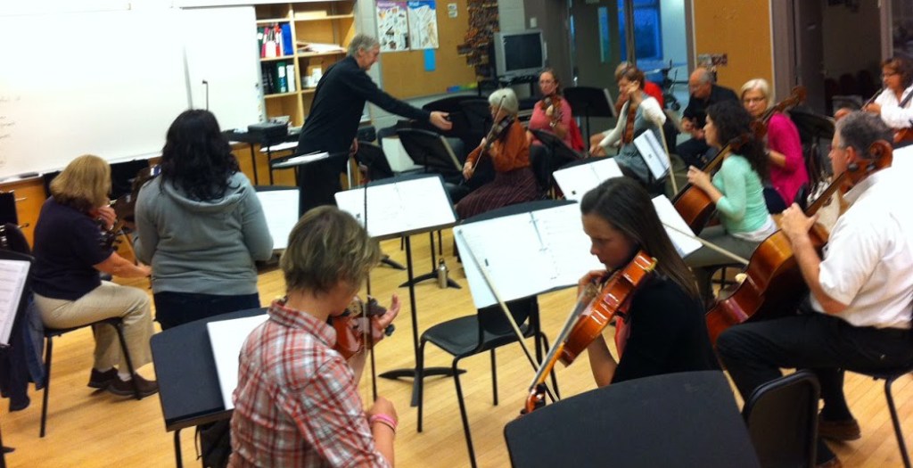Conductor working with the string sections during a rehearsal in a classroom