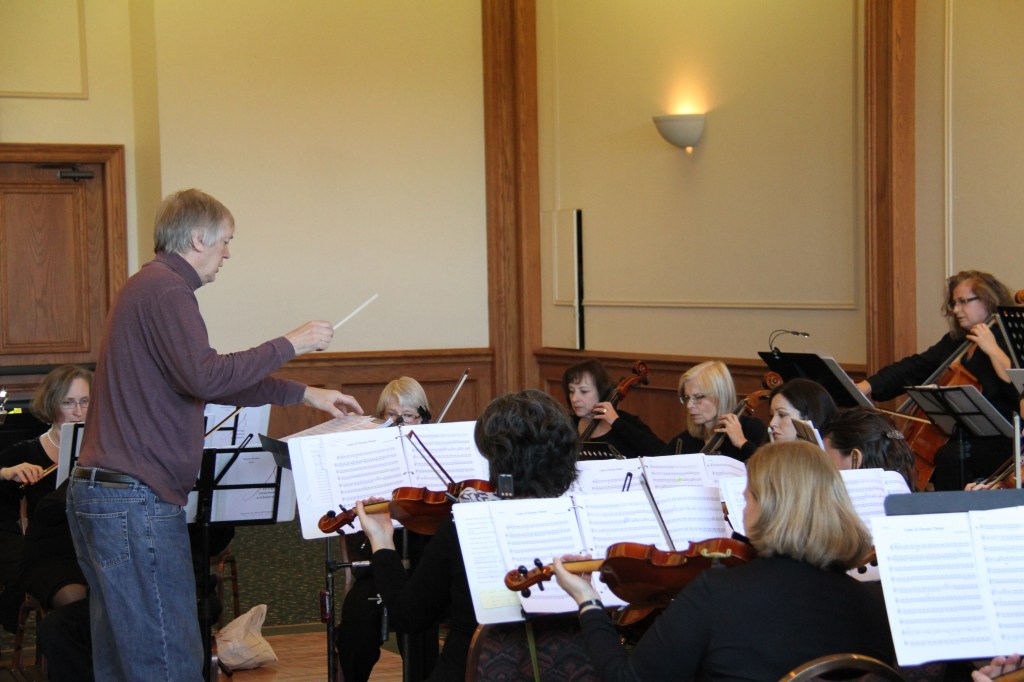 Conductor rehearsing the strings in a hall at Congregation B’nai Torah before the 2014 Holiday Concert