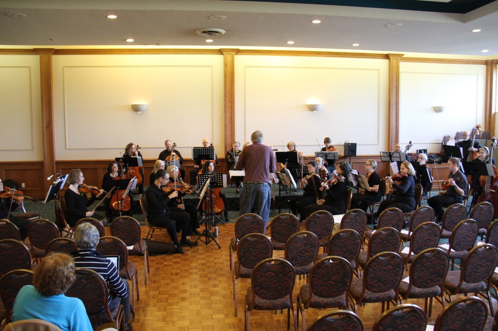 Wide view of the orchestra rehearsing in front of rows of empty chairs before the 2014 Holiday Concert
