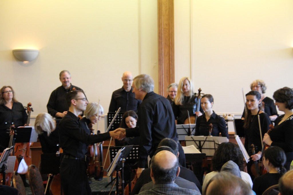 Conductor Matthew Poon congratulating a musician at the front of the orchestra after a piece at the 2014 Holiday Concert