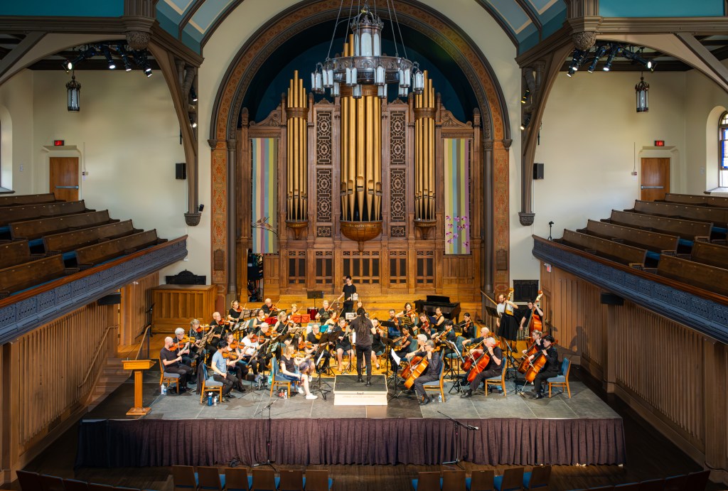 Strings Attached Orchestra performing at Trinity-St. Paul’s Centre, seen from the balcony with the pipe organ behind