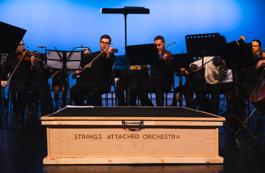 The Strings Attached Orchestra podium in front of the violins