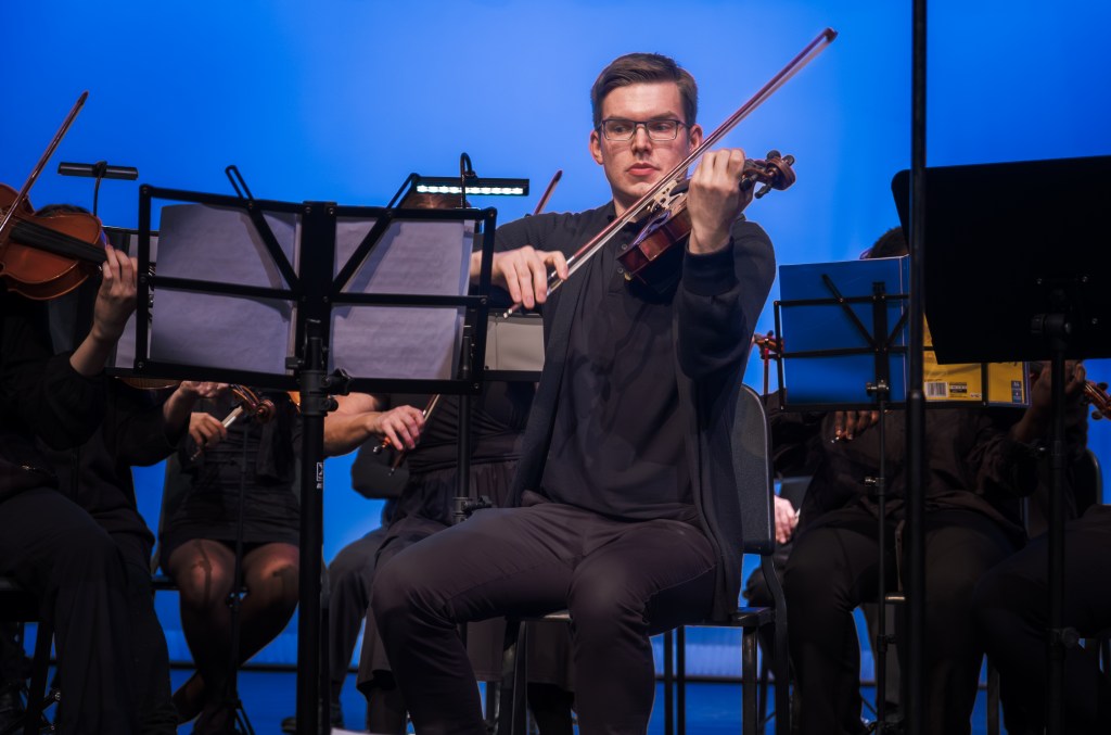 A violinist playing against the blue backdrop
