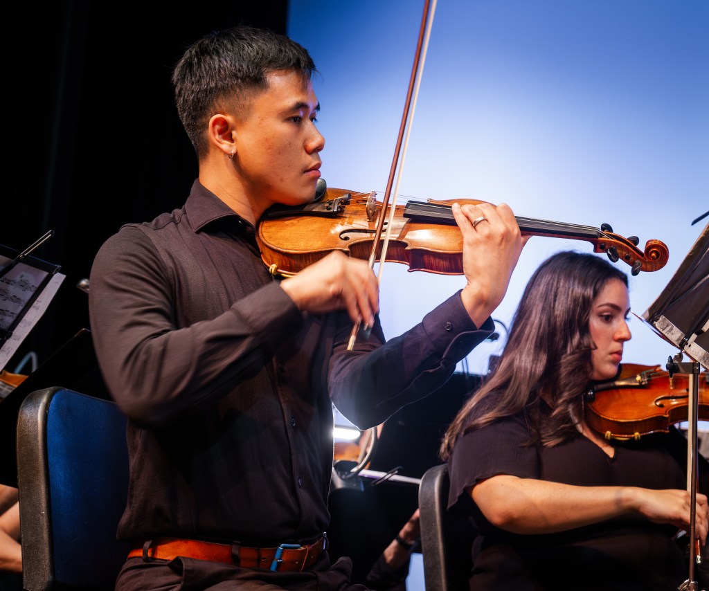 A violinist playing against the blue backdrop