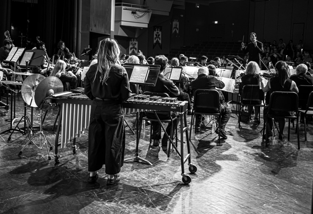 Black-and-white photo of a percussionist playing the marimba beside the orchestra
