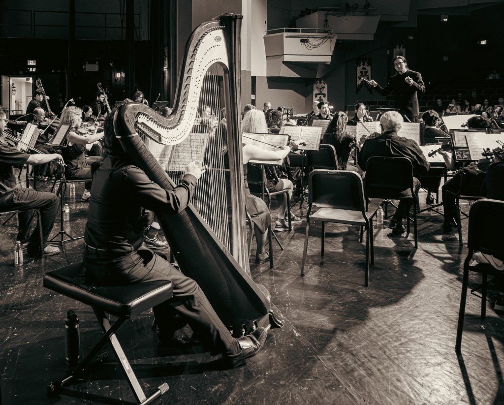 Black-and-white photo of the harp being played beside the orchestra