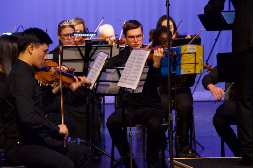 Violin and viola players reading from their stands on a blue-lit stage