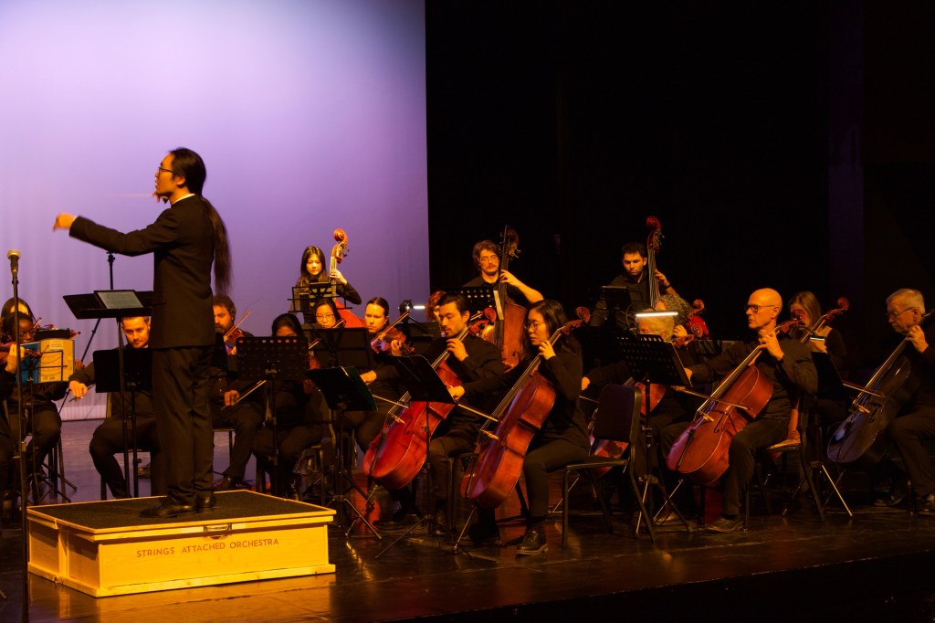 Jonathan Wong conducting the orchestra under warm stage light
