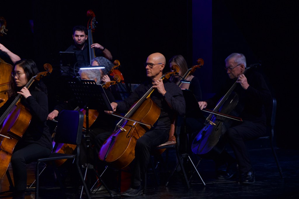 Cellists and double bass players performing on a dark stage