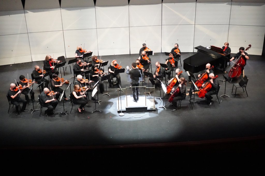The orchestra seated in a semicircle on the MacMillan Theatre stage, seen from above