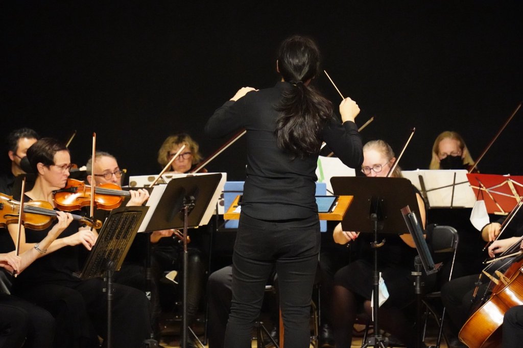 The conductor seen from behind, facing the violins in rehearsal