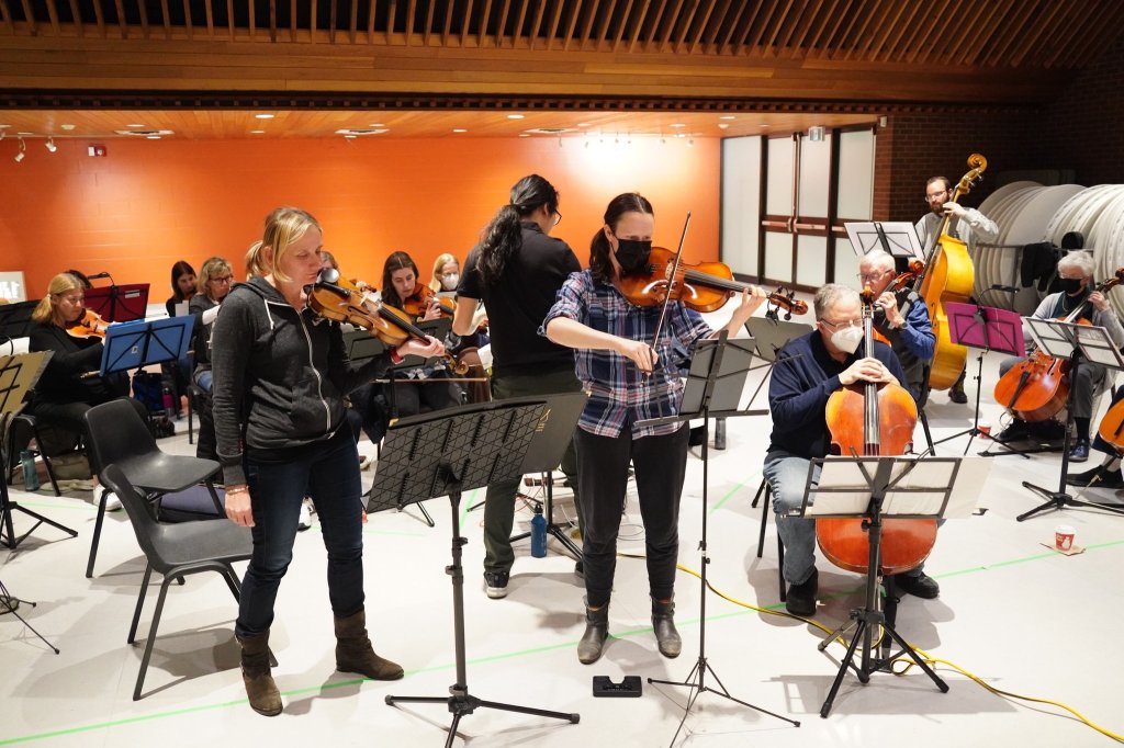 Violinists standing to rehearse with the cellos behind
