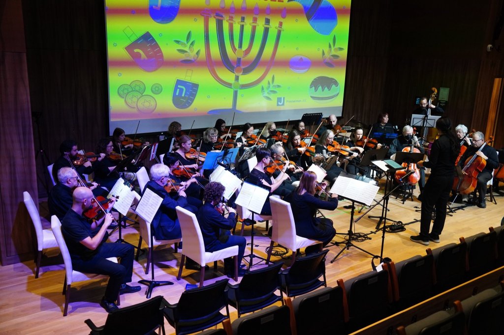 The full orchestra performing beneath a projected menorah at the 2022 Holiday Concert
