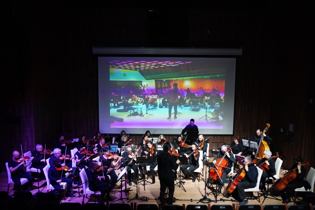 The full orchestra on the Leah Posluns Theatre stage under purple lights