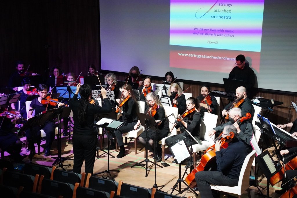 The orchestra and conductor performing in front of a projected holiday image