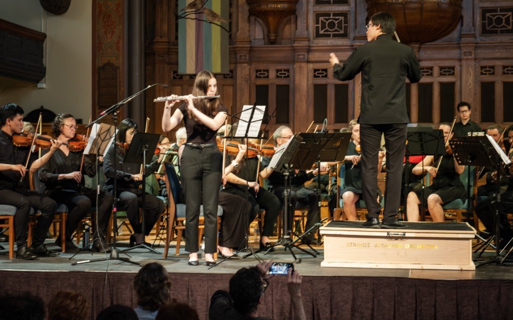 The conductor leading the orchestra in front of the pipe organ