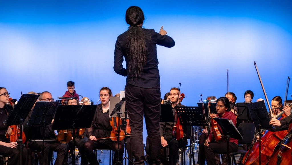 The conductor on the podium against a blue backdrop