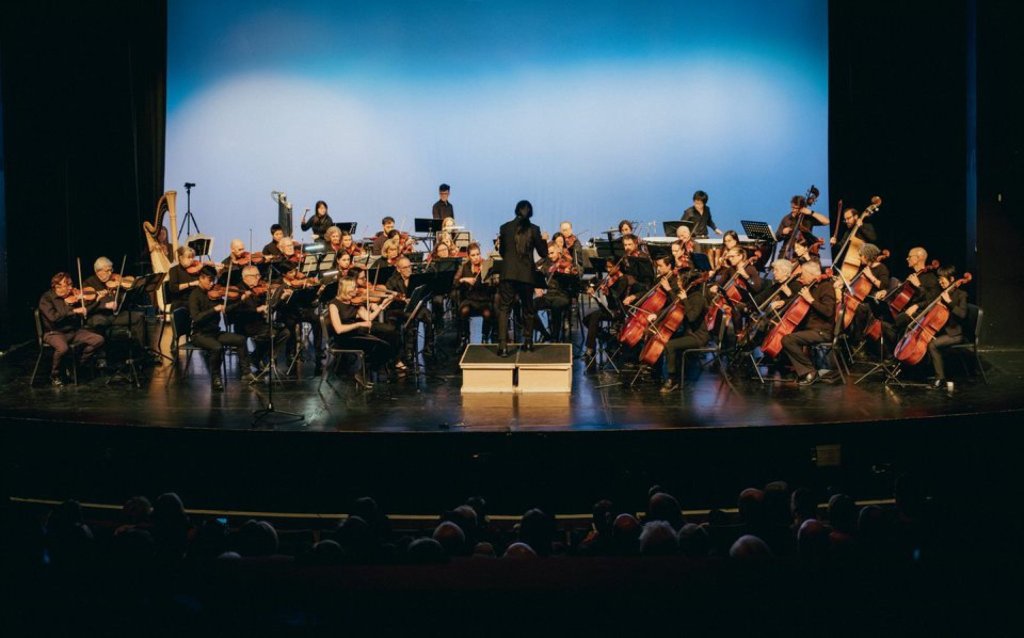 The full orchestra on stage before a blue backdrop